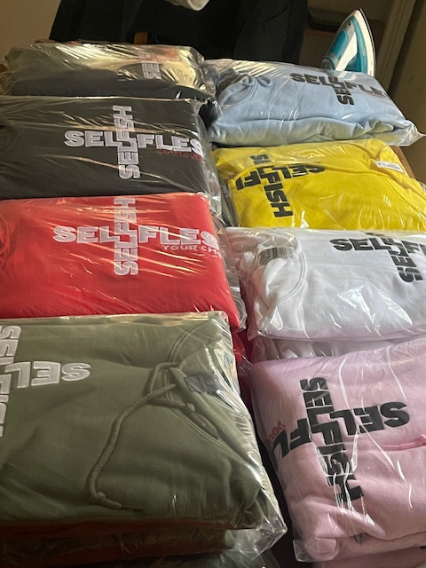 Stack of packaged SSYC unisex hoodies in various colors with embroidered logos visible through plastic wrapping